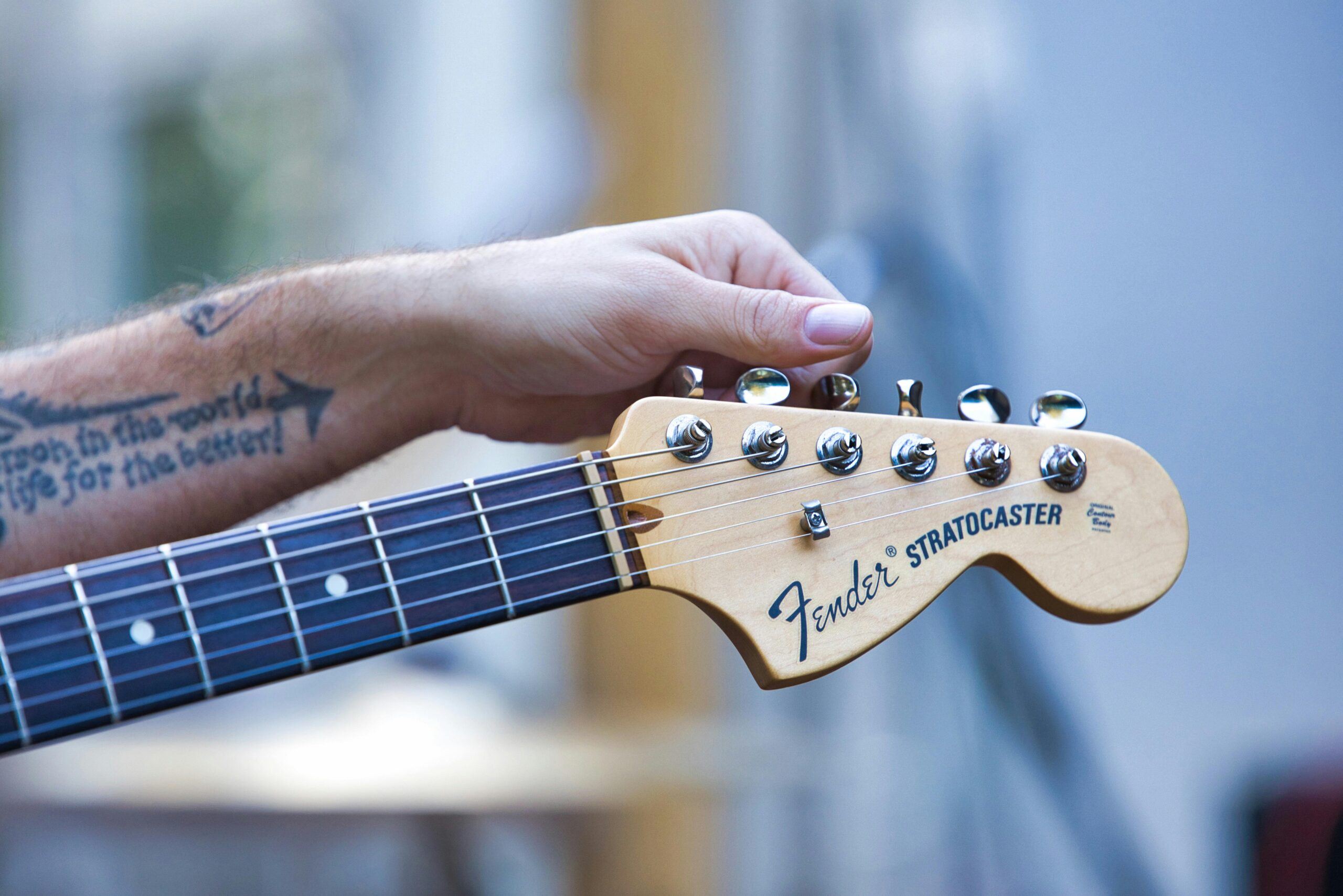 Detailed image of a hand holding a Fender Stratocaster guitar neck with tattoo visible.